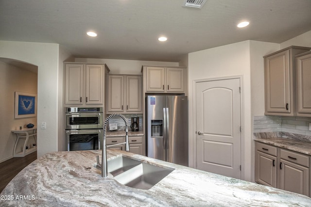 kitchen featuring sink, appliances with stainless steel finishes, dark hardwood / wood-style floors, light stone countertops, and decorative backsplash