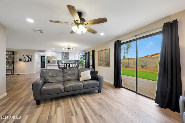 living room with ceiling fan with notable chandelier and light hardwood / wood-style flooring