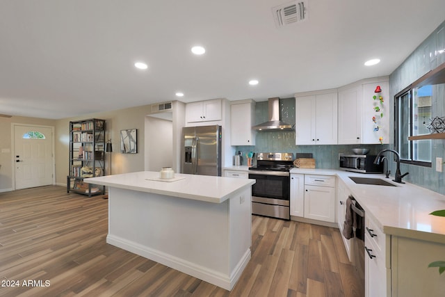 kitchen with white cabinets, wall chimney range hood, sink, wood-type flooring, and stainless steel appliances