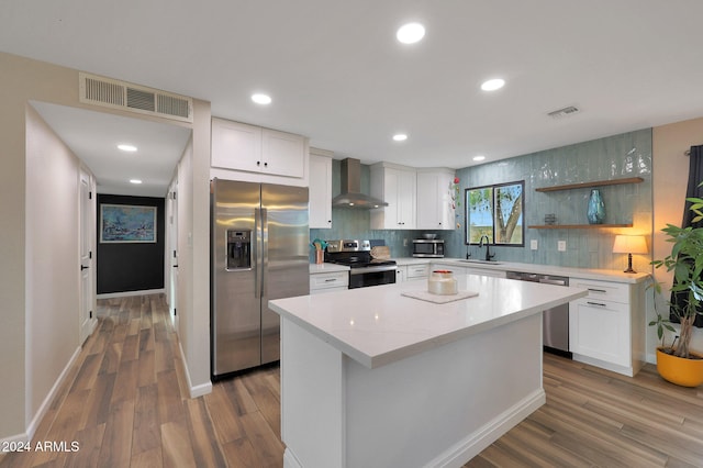 kitchen with wall chimney exhaust hood, stainless steel appliances, white cabinets, hardwood / wood-style floors, and a center island