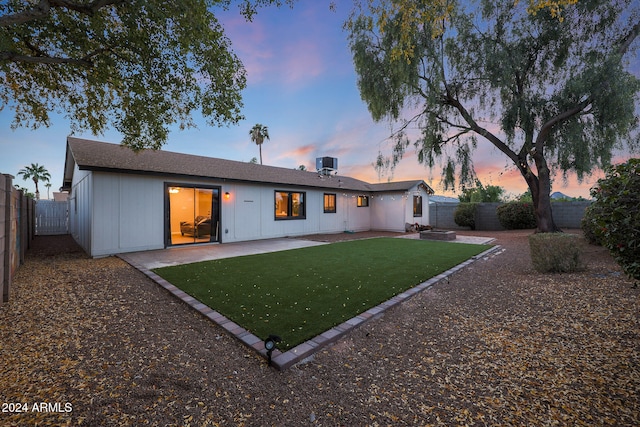 back house at dusk featuring a patio area, a yard, and cooling unit