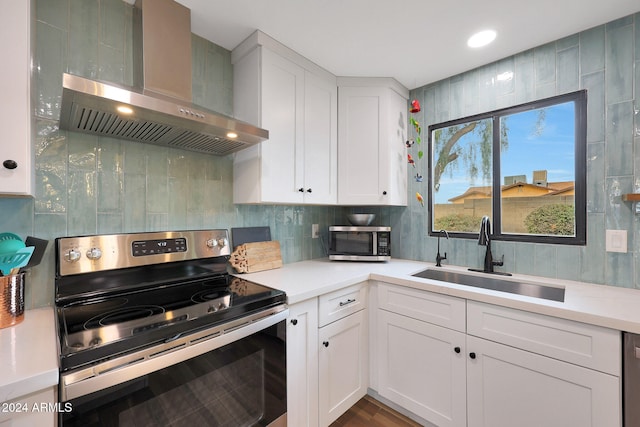 kitchen with sink, wall chimney exhaust hood, white cabinetry, wood-type flooring, and stainless steel appliances