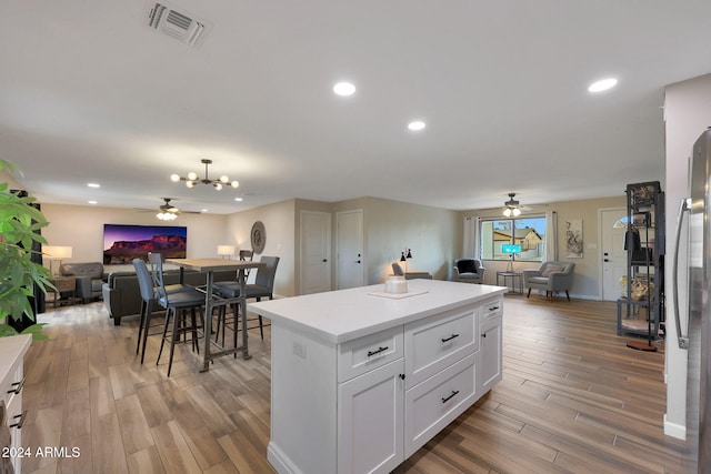 kitchen with stainless steel fridge, white cabinetry, wood-type flooring, and ceiling fan with notable chandelier