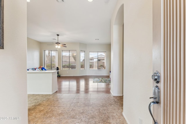 tiled entryway with visible vents, baseboards, arched walkways, and a ceiling fan