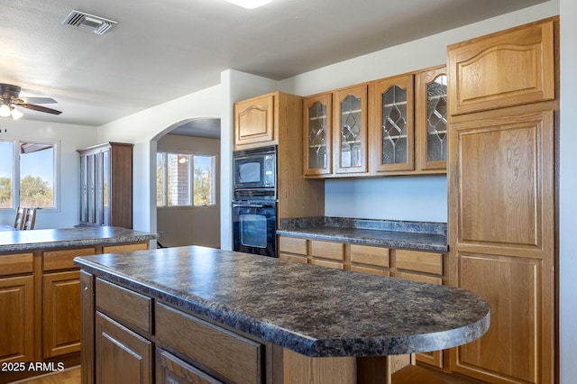 kitchen featuring dark countertops, black appliances, a kitchen island, and glass insert cabinets