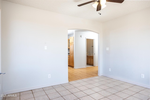 spare room featuring light tile patterned floors, baseboards, arched walkways, ceiling fan, and a textured ceiling