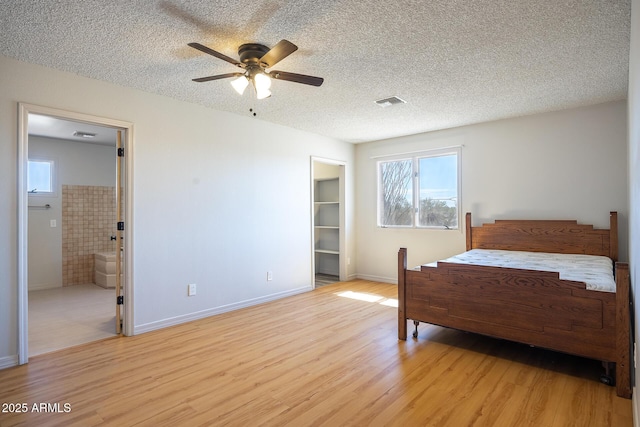 bedroom featuring visible vents, a spacious closet, light wood-style floors, a textured ceiling, and baseboards