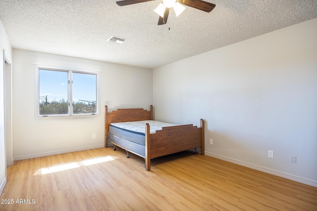 bedroom featuring light wood-style floors, visible vents, baseboards, and a textured ceiling