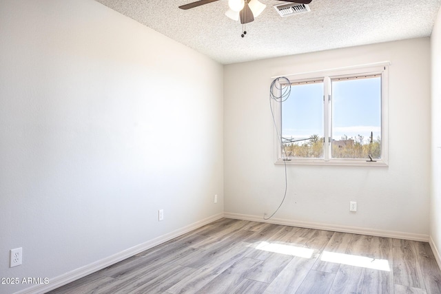 empty room featuring a textured ceiling, light wood-type flooring, visible vents, and baseboards