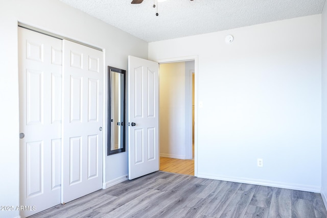 unfurnished bedroom featuring baseboards, a ceiling fan, light wood-style flooring, a textured ceiling, and a closet