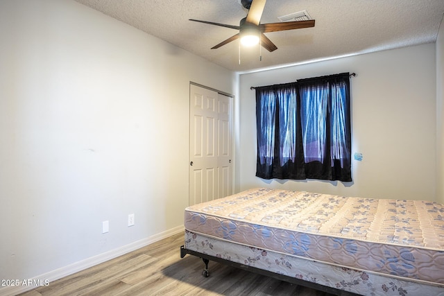 bedroom with a closet, visible vents, a textured ceiling, wood finished floors, and baseboards