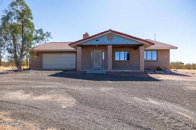 single story home with driveway, a chimney, an attached garage, and a tile roof