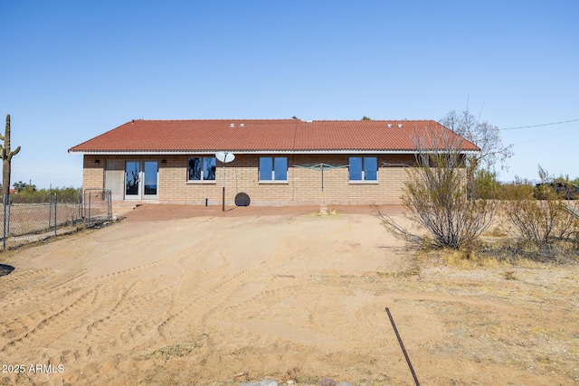 back of house featuring dirt driveway, brick siding, a tile roof, and fence