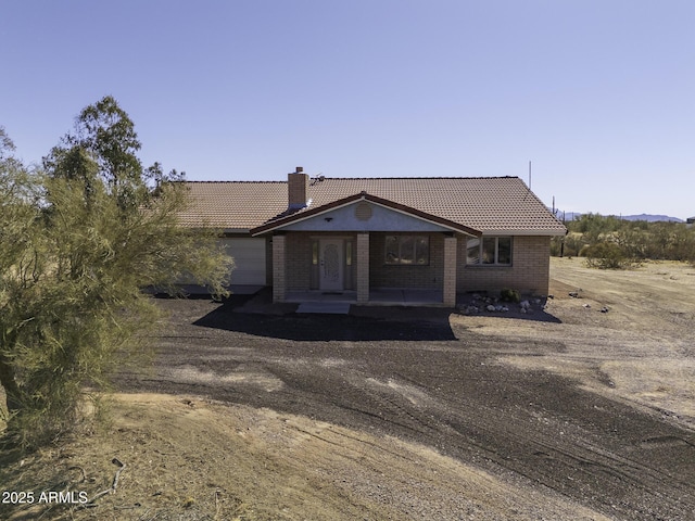 ranch-style home with a chimney, a tiled roof, an attached garage, a patio area, and brick siding