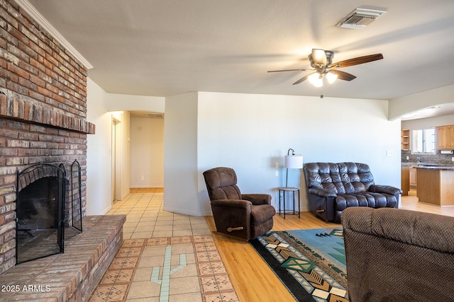 living room featuring visible vents, arched walkways, a ceiling fan, light wood-style flooring, and a fireplace