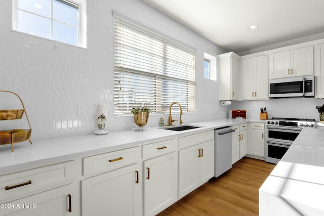 kitchen featuring light stone countertops, appliances with stainless steel finishes, sink, light hardwood / wood-style floors, and white cabinetry