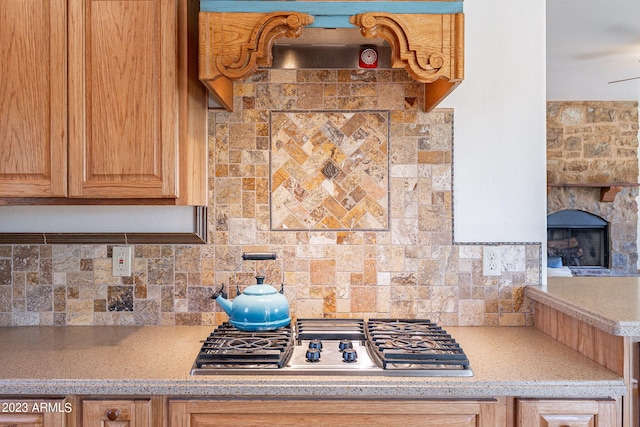 kitchen featuring backsplash, a stone fireplace, and stainless steel gas cooktop