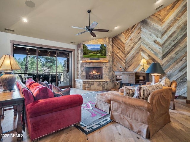 living room featuring vaulted ceiling, hardwood / wood-style floors, a fireplace, wood walls, and ceiling fan