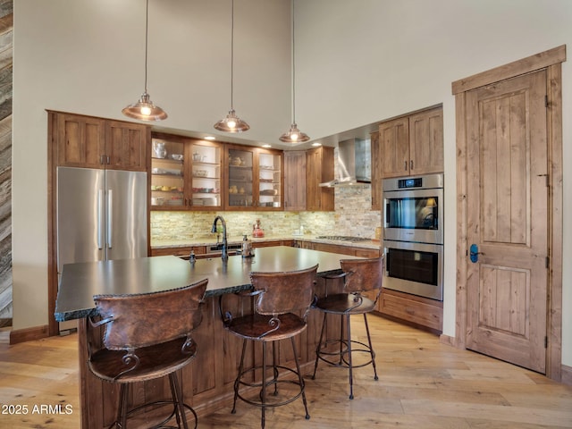 kitchen with tasteful backsplash, wall chimney range hood, an island with sink, and appliances with stainless steel finishes