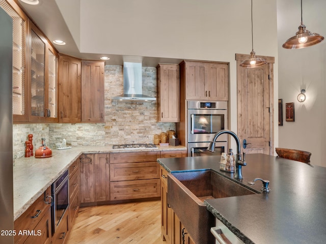 kitchen featuring pendant lighting, wall chimney range hood, sink, appliances with stainless steel finishes, and backsplash