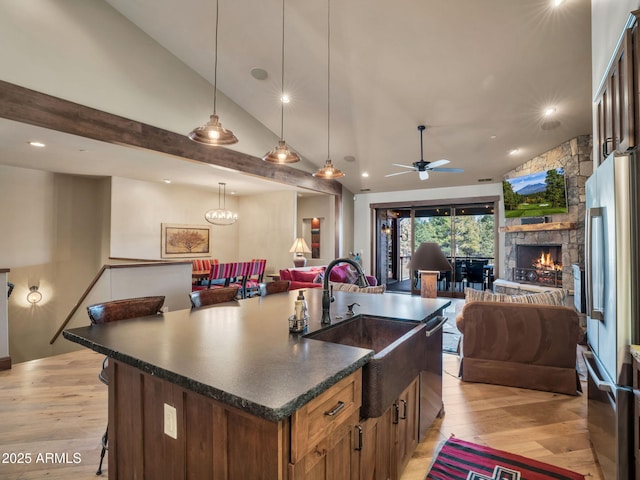 kitchen with a breakfast bar, pendant lighting, an island with sink, sink, and stainless steel fridge