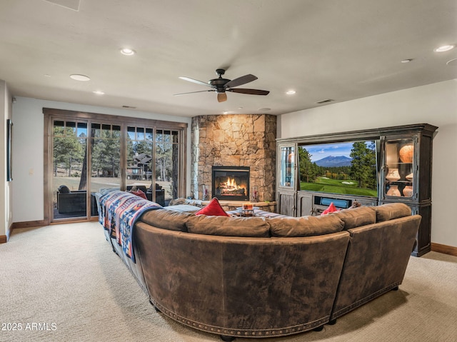 carpeted living room featuring ceiling fan, a stone fireplace, and a healthy amount of sunlight