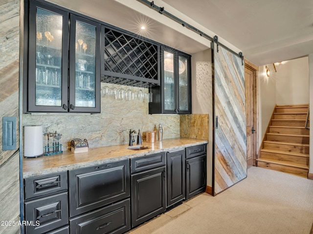 bar featuring a barn door, sink, light colored carpet, and light stone counters