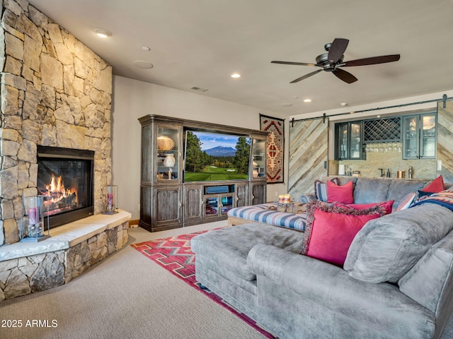 carpeted living room with ceiling fan, a fireplace, and a barn door