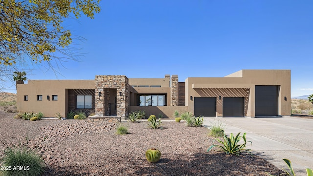 pueblo-style home featuring stucco siding, a garage, driveway, and stone siding