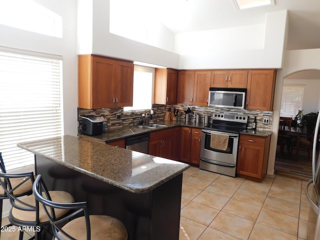 kitchen with kitchen peninsula, a kitchen breakfast bar, stainless steel appliances, and high vaulted ceiling