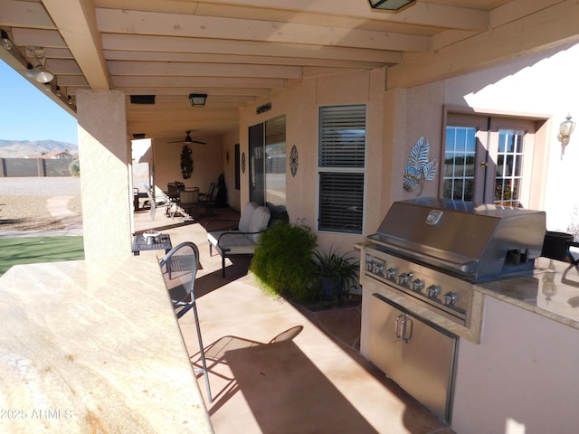 view of patio featuring a mountain view, a grill, ceiling fan, and an outdoor kitchen