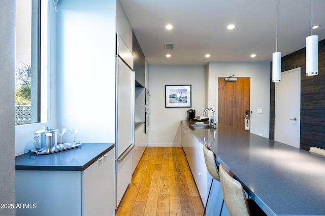 kitchen with sink, pendant lighting, white cabinets, and light wood-type flooring