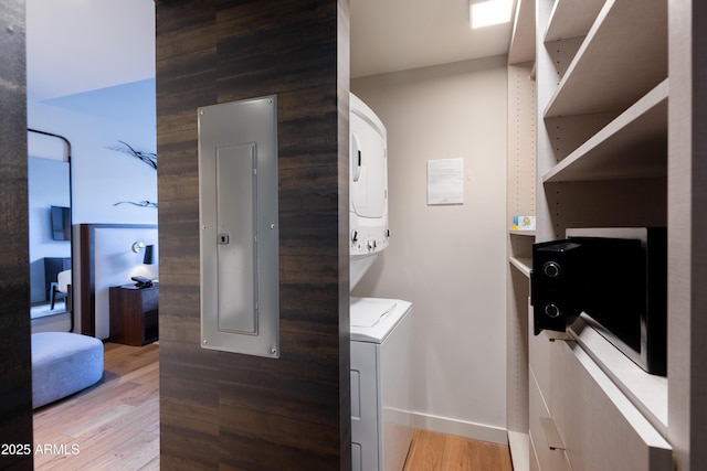 clothes washing area featuring stacked washer / dryer, wood-type flooring, and electric panel