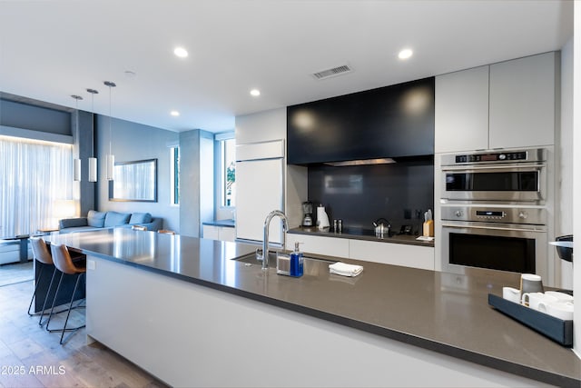 kitchen with sink, decorative light fixtures, light hardwood / wood-style flooring, double oven, and a wealth of natural light