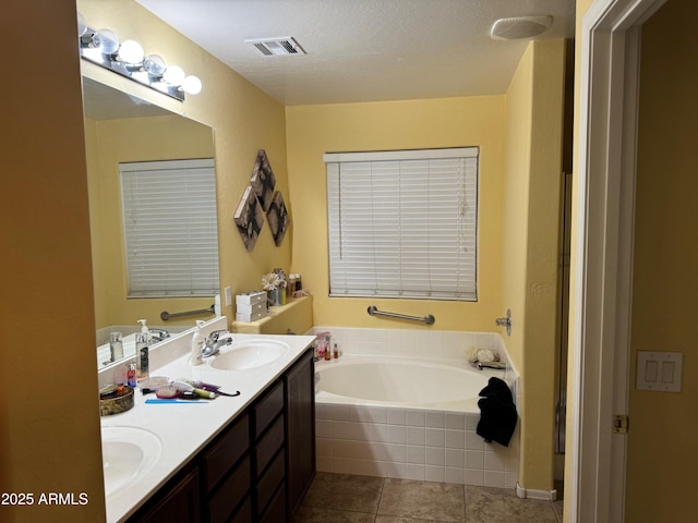 bathroom featuring tile patterned flooring, visible vents, double vanity, a bath, and a sink