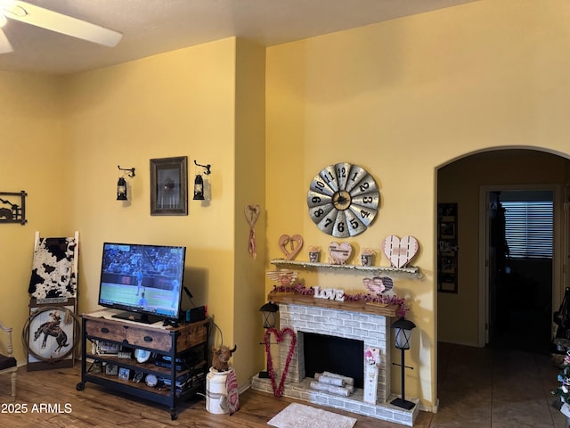 living area with wood finished floors, arched walkways, ceiling fan, and a fireplace