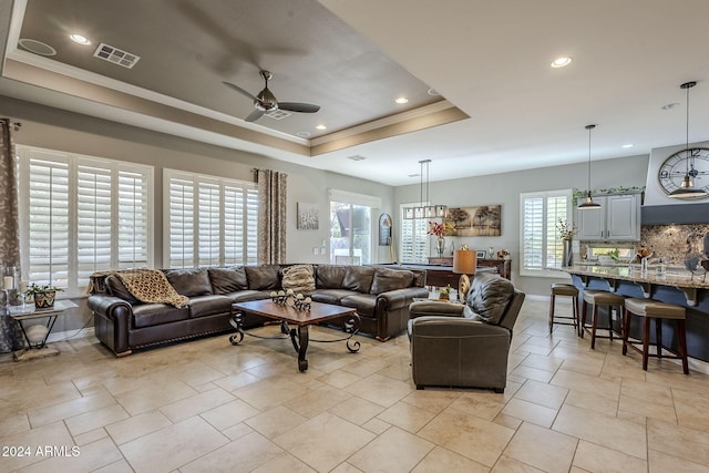 living room featuring a raised ceiling, ceiling fan, and ornamental molding