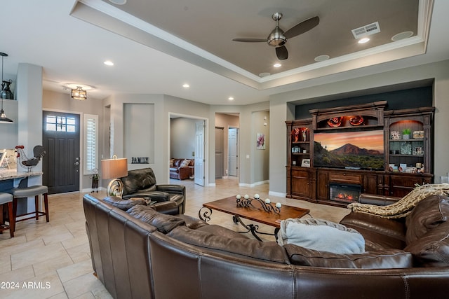 living room with ceiling fan, a raised ceiling, and crown molding