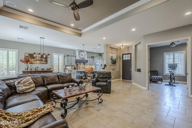 living room featuring plenty of natural light, ceiling fan, a raised ceiling, and crown molding