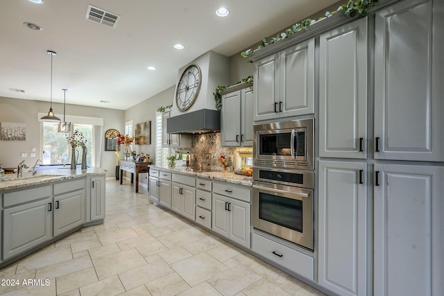 kitchen featuring gray cabinetry, light stone countertops, stainless steel appliances, tasteful backsplash, and decorative light fixtures