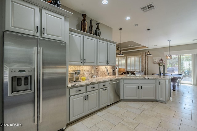 kitchen with pendant lighting, decorative backsplash, appliances with stainless steel finishes, light stone counters, and kitchen peninsula