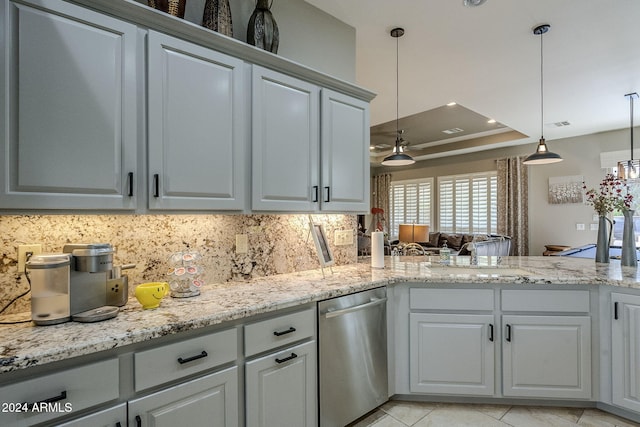 kitchen with pendant lighting, backsplash, a raised ceiling, stainless steel dishwasher, and light stone counters