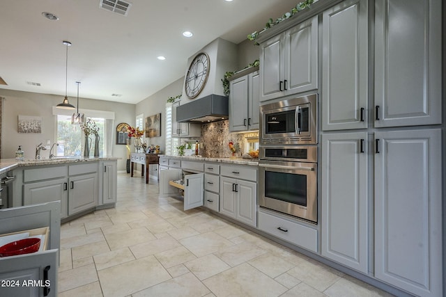 kitchen featuring stainless steel appliances, gray cabinets, tasteful backsplash, and light stone counters