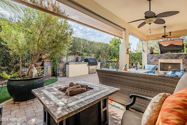 view of patio with an outdoor kitchen, ceiling fan, grilling area, an outdoor fire pit, and a tiled fireplace