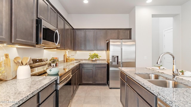 kitchen with a sink, recessed lighting, dark brown cabinetry, appliances with stainless steel finishes, and light stone countertops