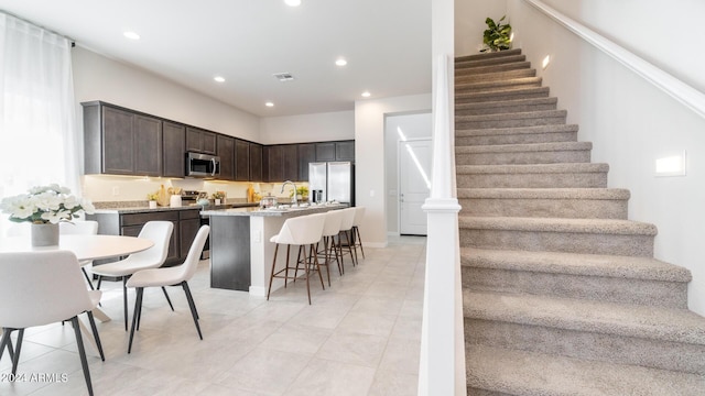 interior space with visible vents, a sink, stainless steel appliances, dark brown cabinetry, and a kitchen bar