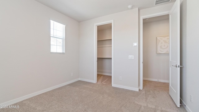 unfurnished bedroom with a walk in closet, light colored carpet, visible vents, and baseboards