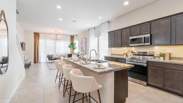 kitchen featuring a center island with sink, a sink, stainless steel appliances, a breakfast bar area, and dark brown cabinets