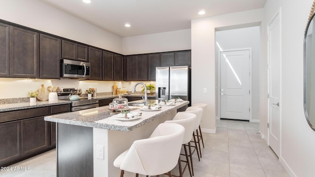 kitchen with dark brown cabinetry, a center island with sink, a kitchen bar, recessed lighting, and appliances with stainless steel finishes