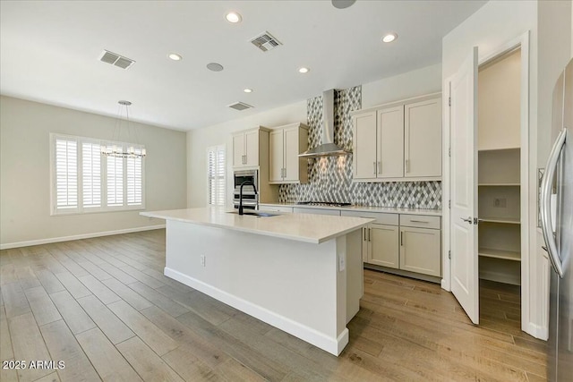 kitchen with pendant lighting, wall chimney range hood, decorative backsplash, and an island with sink